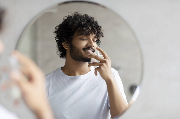 Elégedett indiai férfi illata parfüm, csinál reggeli szépség rutin, élvezi a kellemes illat, áll a fürdőszobában - Fotó, kép