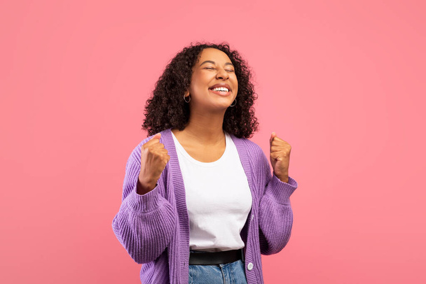 Приємна афроамериканська жінка робить жест YES, відзначаючи величезну перемогу на рожевому фоні студії - Фото, зображення