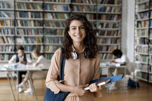 Happy Hispanic gen Z student girl with headphones visiting library - Fotoğraf, Görsel