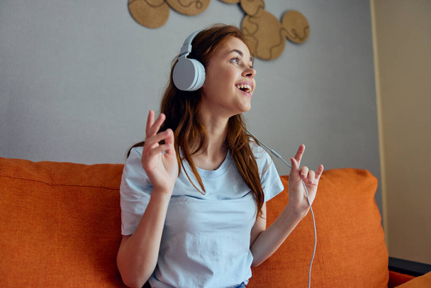 csinos nő hallgat zenét fülhallgató a narancssárga kanapé apartmanok - Fotó, kép