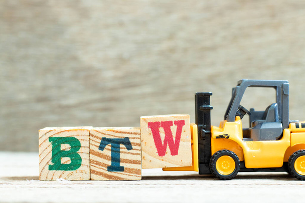 Carretilla elevadora de juguete mantenga el bloque de letras W para completar la palabra BTW (Abreviatura de por cierto) sobre fondo de madera - Foto, imagen