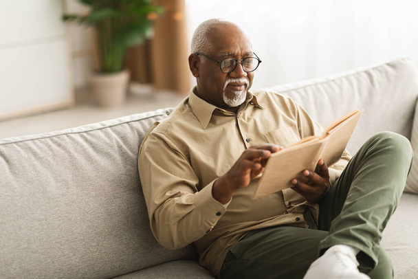 Mature Black Man Reading A Book Relaxing Sitting At Home - Фото, изображение