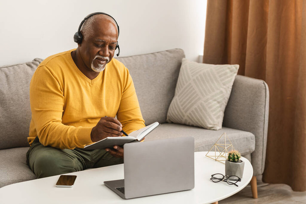 Olgun Siyah Bağımsız Adam dizüstü bilgisayar kullanarak evde not alıyor. - Fotoğraf, Görsel