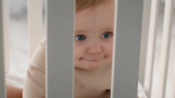 Adorabile bambino piccolo sbirciando fuori mentre seduto all'interno del lettino per bambini - Filmati, video
