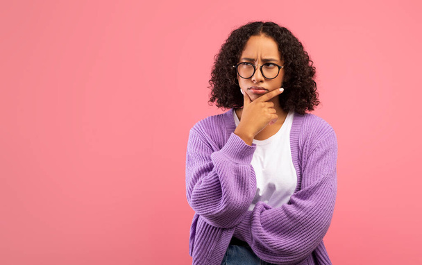 Portrait of pensive African American woman touching chin and looking at free space on pink studio background - Photo, Image