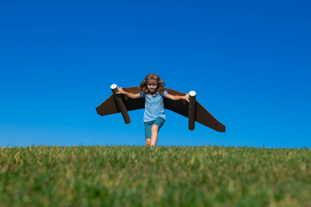 Happy child playing outside on green grass and blue sky. Kid pilot with toy jetpack. Kid boy play with toy plane cardboard. Summer travel and adventure. Success winner, imagination and dream concept. - Photo, Image