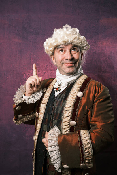 Adult man in classical renaissance clothing pointing up with finger showing something. - Foto, Bild