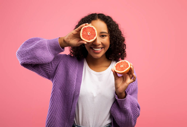 Happy black woman holding cut grapefruit on pink studio background. Fruit vitamins and detox concept - Φωτογραφία, εικόνα