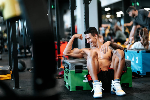 Portrait of smiling man during workout pause at gym, flexing biceps muscles - Fotó, kép