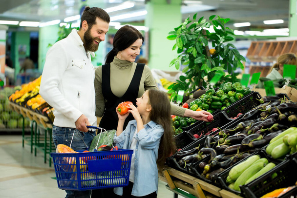 a woman with a man and a child, choosing vegetables while shopping in a vegetable supermarket. - Foto, Imagen