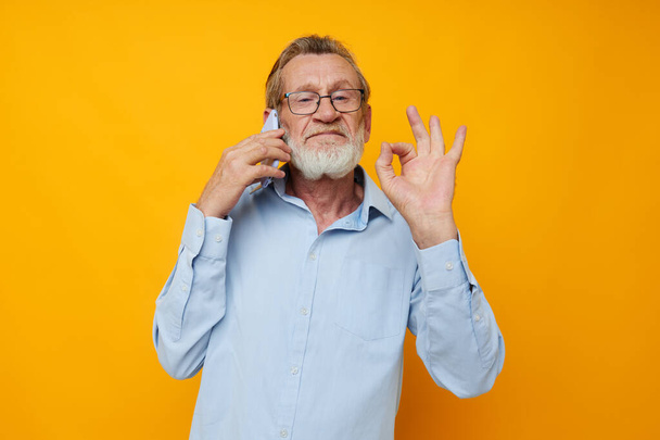 Portrait elderly man in a blue shirt and glasses talking on the phone unaltered - Foto, Imagen