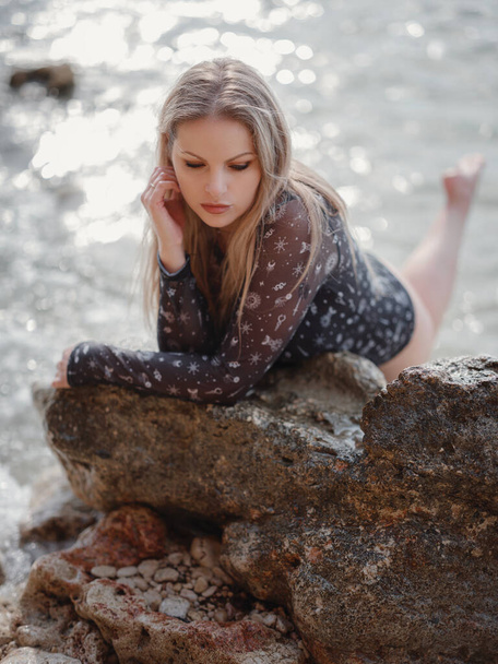 Portret van een aantrekkelijke Amerikaanse blonde vrouw met lang haar poserend op rotsachtig strand. Mooi pluspunt - Foto, afbeelding