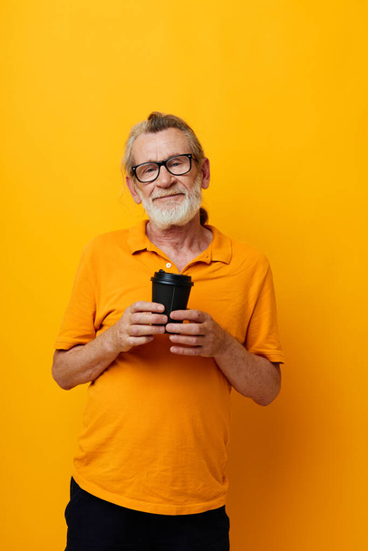 elderly man in a yellow T-shirt a glass with a drink yellow background - Foto, Imagen