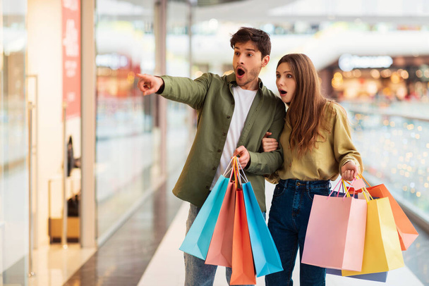 Erstaunt Paar Doing Shopping Pointing Finger Neben In Mall - Foto, Bild