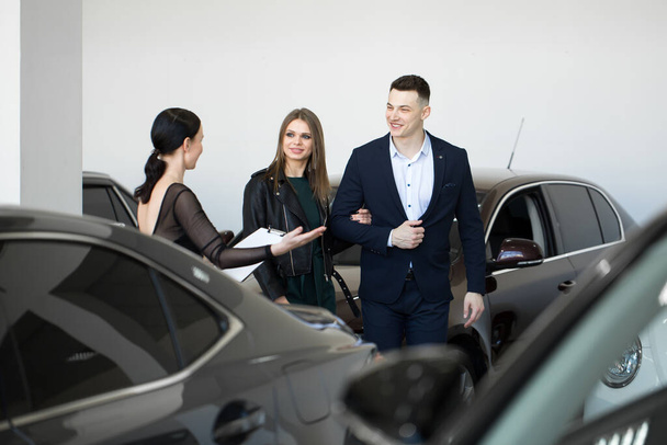 auto business, car sales - a happy couple with a car dealer in a car dealership or salon. - Fotografie, Obrázek