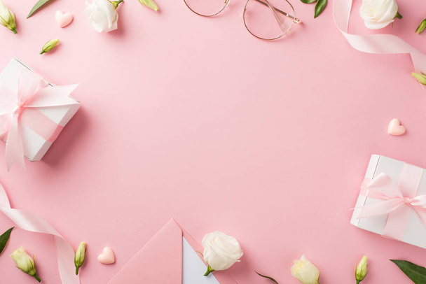 Bovenaanzicht foto van vrouw dag samenstelling cadeau dozen roze lint envelop met brief stijlvolle glazen harten en prairie gentiaan bloemen op geïsoleerde pastel roze achtergrond met copyspace in het midden - Foto, afbeelding