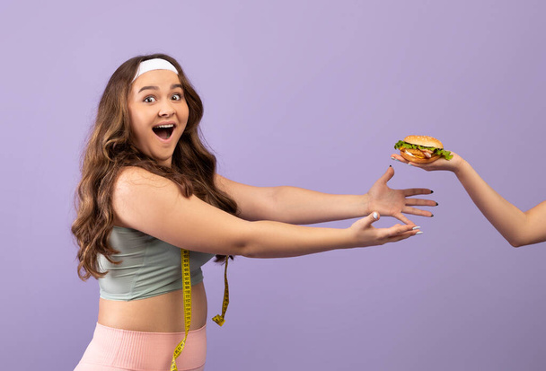Verrast blij hongerig Kaukasisch plus size jonge dame in sportkleding met open mond wil hamburger te nemen - Foto, afbeelding