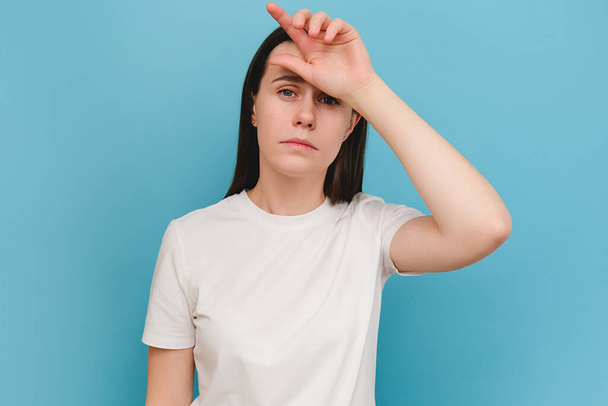 Portrait of tired sad young brunette woman suffering from headache, isolated on blue background with copy space. Cause of headache include migraine, tension headache, stress, depression or brain tumor - Valokuva, kuva