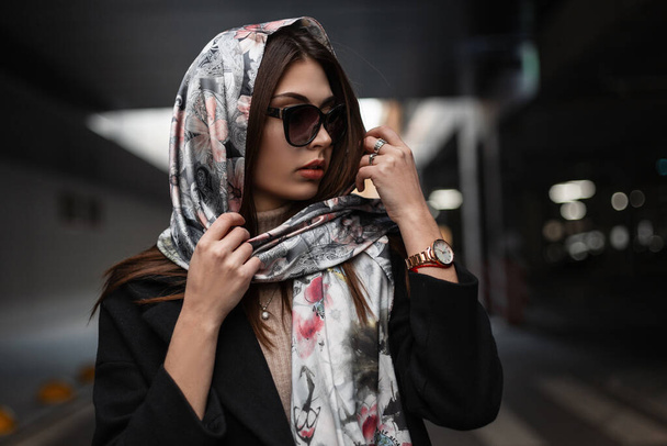 Stylish portrait young European woman with sexy beautiful lips in trendy sunglasses in coat with elegant silk scarf on head in the city. Modern business girl fashion model. Retro fashion. Beauty lady. - Photo, Image