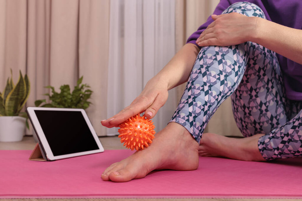 the girl sits and massages herself with a ball to relax, looks at the tablet - Photo, Image
