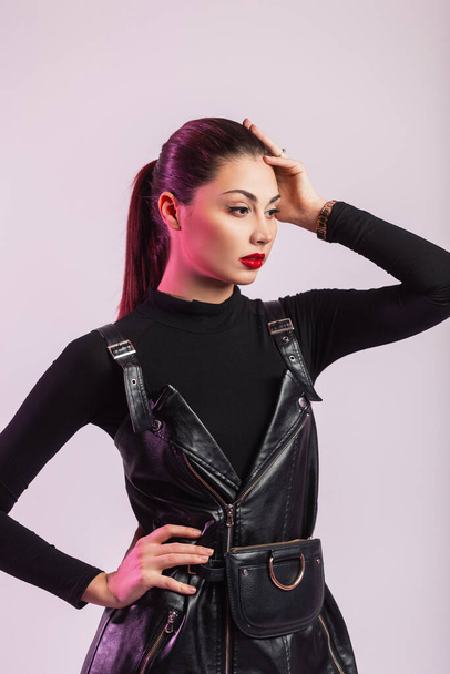 Studio portrait glamorous young woman with clean skin with sexy red lips in fashionable black leather clothes with trendy hairstyle in the room. Stylish cute girl model posing indoors. Retro fashion. - Φωτογραφία, εικόνα