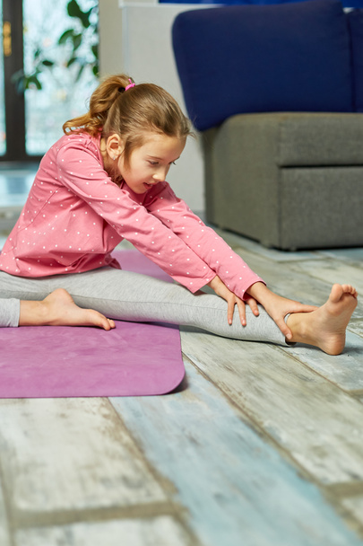 Little girl doing stretching exercises, practicing yoga on fitness mat at home, Playing sports, Healthy lifestyle. Kids sport home quarantine - Фото, зображення