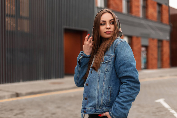 Fashion model american young pretty hipster woman in stylish denim jacket walks in the city. Fashionable urban girl in jeans clothes outdoors. Casual style. Youth street look. Spring wear for women. - Фото, изображение