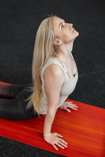 Professionelle junge Frau macht Übungen für den Rücken im Fitnessraum auf der Matte. Mädchen praktizieren Yoga, Stretching oder Pilates. Sportlicher Lebensstil. - Foto, Bild