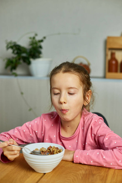 Cute little girl enjoy eating cereal with milk for morning breakfast with appetite, How tasty healthy food, Slow motion of beautiful child having breakfast at home. - Foto, afbeelding