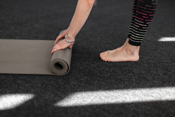 Young woman stands barefoot and unfolds a sports mat for training. Close-up. - Photo, Image