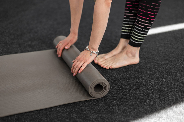 Treinador jovem em leggings fica descalço e desdobra um tapete esportivo para ioga. Close-up. - Foto, Imagem