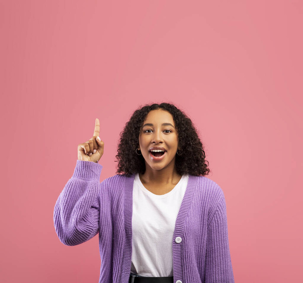 Возбужденная черная женщина, указывающая вверх на пространство для копирования, имеющая творческую идею или вдохновение на розовом фоне студии - Фото, изображение