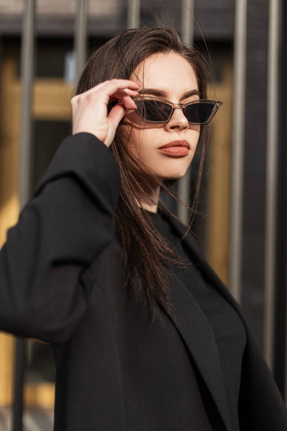 Portret mooie charmante jonge vrouw met sexy lippen in zwarte modieuze kleding op zonsondergang achtergrond. Aantrekkelijk meisje mode model. - Foto, afbeelding