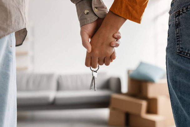 Großaufnahme eines jungen Paares, das sich an Händen und neuem Hausschlüssel hält und zusammen einzieht. Hypothek, Immobilienkonzept - Foto, Bild