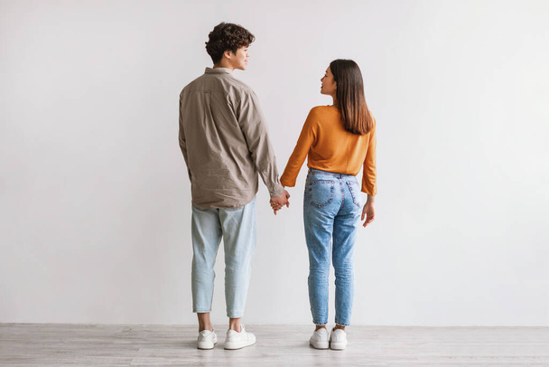 Full length of young Asian man and woman standing with their backs to camera, looking at each other and holding hands - Foto, Imagem