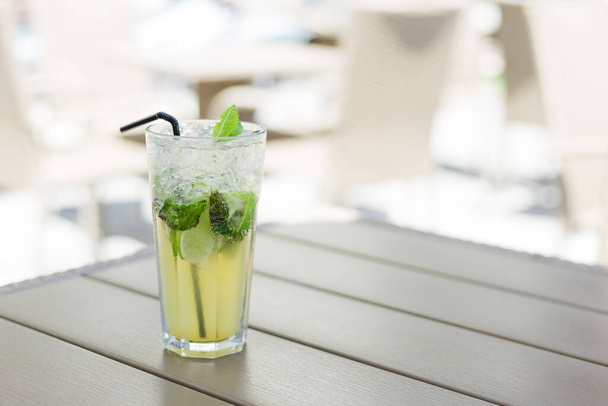 Glass of Lemonade or mojito cocktail with lemon and mint, cool refreshing drink or beverage, outdoor. Cold detox water with ice and straw, copy space. - Φωτογραφία, εικόνα