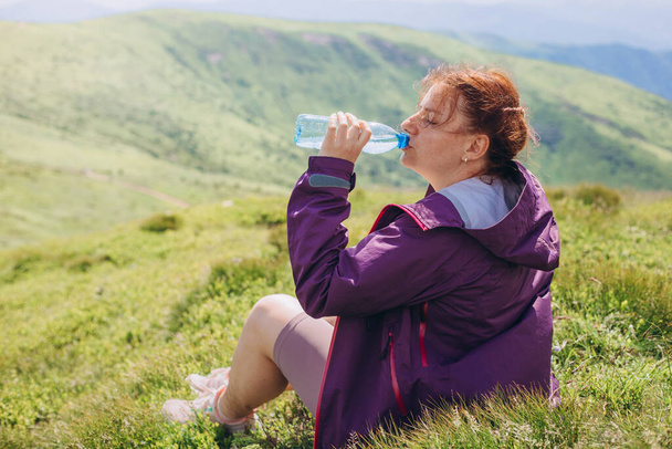 Gyönyörű Női turista inni vizet magas csúcsok Csodálatos kilátás. Szabadság, boldogság, utazás és nyaralás koncepció. Egy üveg tiszta ivóvíz műanyag palackban a hegyekben. - Fotó, kép