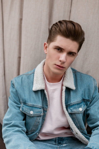 Vogue European nice young man with clean skin with stylish hairstyle in trendy blue denim jacket is relaxing outdoors in city. Handsome guy fashion model in fashionable clothes. Street style. - Foto, Imagem