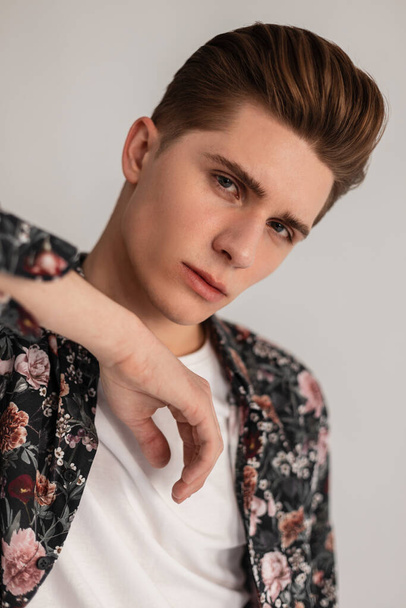 Fresh portrait young European trendy man with hairstyle with serious face in white T-shirt in elegant stylish floral print shirt in studio. Attractive pretty handsome fashionable guy indoors. Close-up - Foto, afbeelding