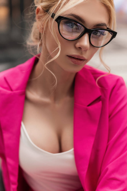 Μοντέρνο πορτρέτο χαριτωμένο ξανθιά νεαρή γυναίκα σε κομψό κομψό κομψό ροζ σακάκι σε μοντέρνα γυαλιά με χτένισμα με εκπληκτικά χείλη σε εσωτερικούς χώρους. Ελκυστικό, όμορφο κορίτσι μοντέλο. Σέξι επιχειρηματίας.. - Φωτογραφία, εικόνα