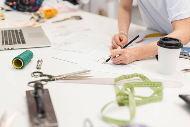 Fashion Designer Stylish Showroom Concept Женщина рисует эскиз модной новой одежды. Профессиональное рабочее пространство с ноутбуком, нитками, ножницами, сантиметром, кофе и другими инструментами для шитья. - Фото, изображение