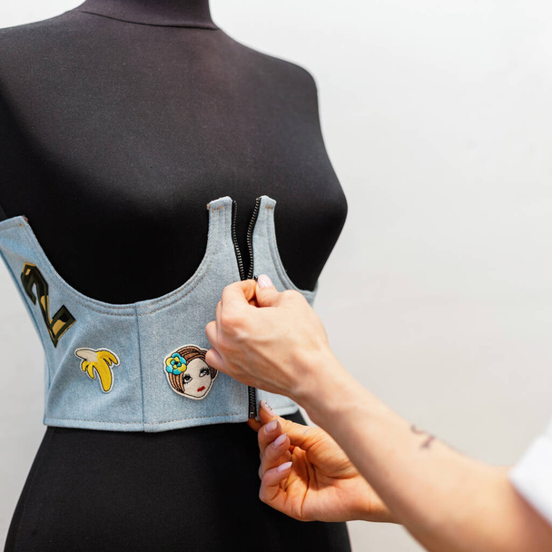 Ženské ruce nosí stylovou džínovou vestu na černé figuríně. Koncept práce jako módní návrhář ve studiu - Fotografie, Obrázek