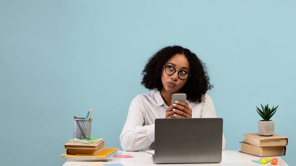 Jeune femme noire réfléchie assise au bureau avec ordinateur portable et smartphone, regardant de côté l'espace vide, la conception de bannière - Photo, image