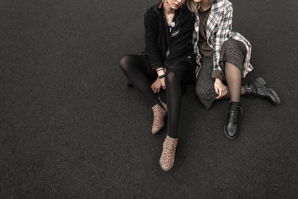 Fashionable feminine style concept. Two beautiful pretty young women in a stylish coat, trousers. skirt with tights and shoes sitting on the pavement. Leopard print boots - 写真・画像