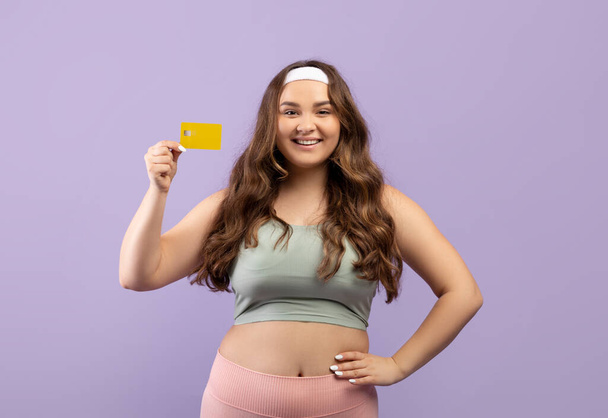 Mosolygó kaukázusi plusz mérete fiatal nő sportruházat mutatja hitelkártya és fizetni edzőterem - Fotó, kép