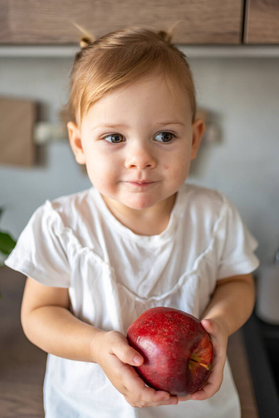 Niña rubia comiendo una manzana en la cocina, concepto de comida saludable para niños - Foto, Imagen