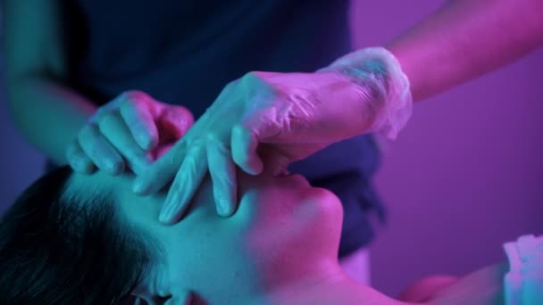 Séance de massage - femme thérapeute massant le visage de sa cliente avec ses doigts - éclairage violet - Séquence, vidéo