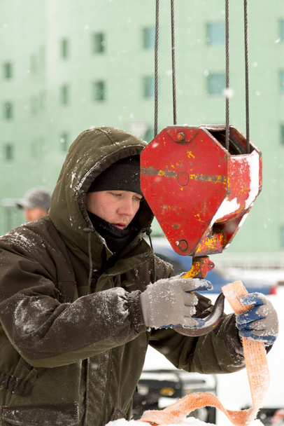 Портрет працівника в зеленій куртці з капюшоном на гачку крана вантажівки завантаження крижаних блоків
 - Фото, зображення