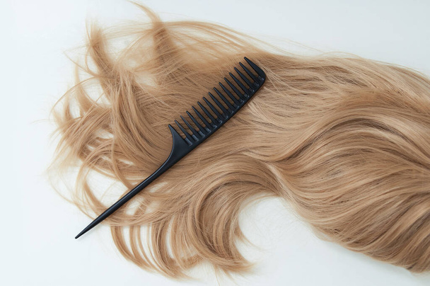 Long blond hair and black comb on a white background. - Photo, Image