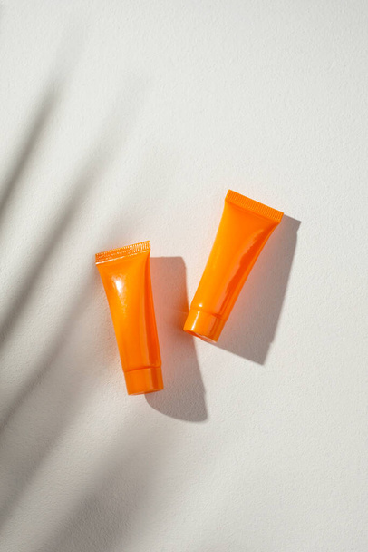 Plastic orange bottles for cream or lotion on a white background. Skin care cosmetic with beautiful palm shadows. Beauty concept for face body care. Place for text - Fotó, kép